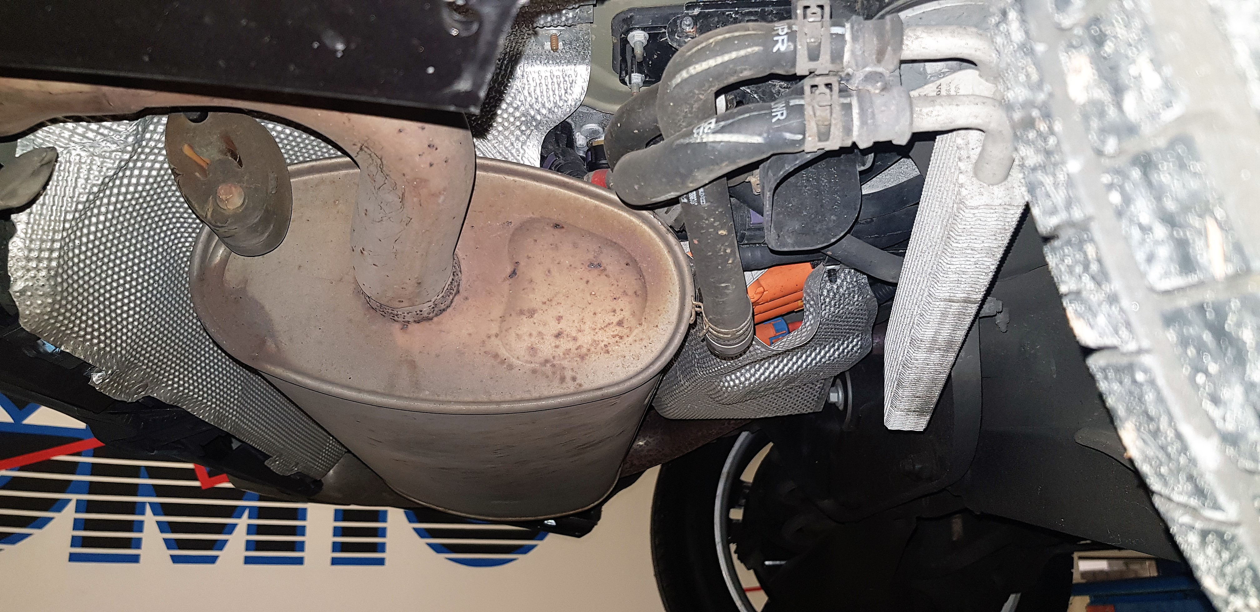 Blik onder de hybride Volvo. Bij de aanrijding is de uitlaat tegen de oranje stekker van de inverter aangeduwd.