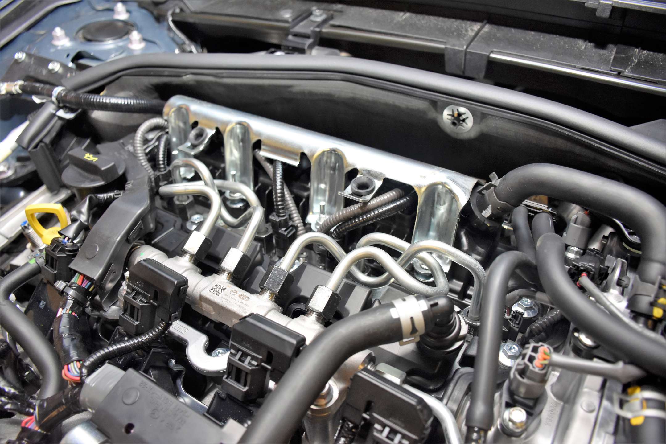 Blik op de SkyActiv X-motor. Onder in beeld de penbobines. Merk op dat die schuin de motor insteken. De injectoren zitten op enige afstand. “Ten opzichte van de SkyActiv G-motor wisselden bougie en injector van plaats”, weten de TTA-trainers. “De bougie zit nu aan de zijkant.”