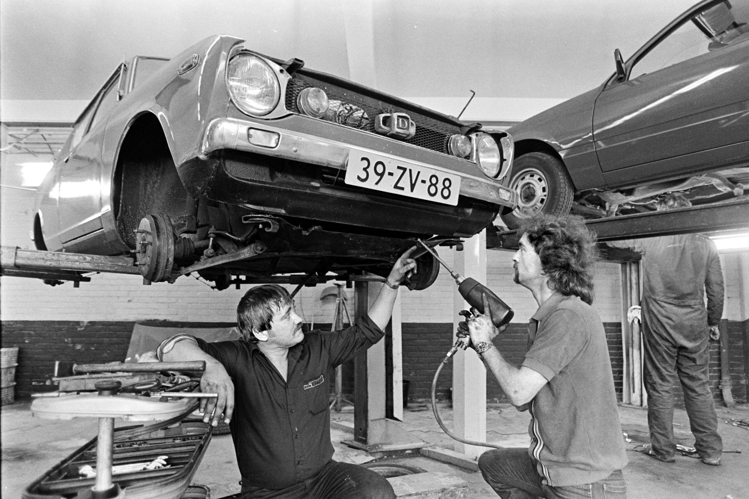 Een doe-het-zelf-garage in Amsterdam, in 1983. De chef werkplaats leert de klant hoe hij zelf een reparatie uitvoert. - Foto: ANP / Bert Verhoeff